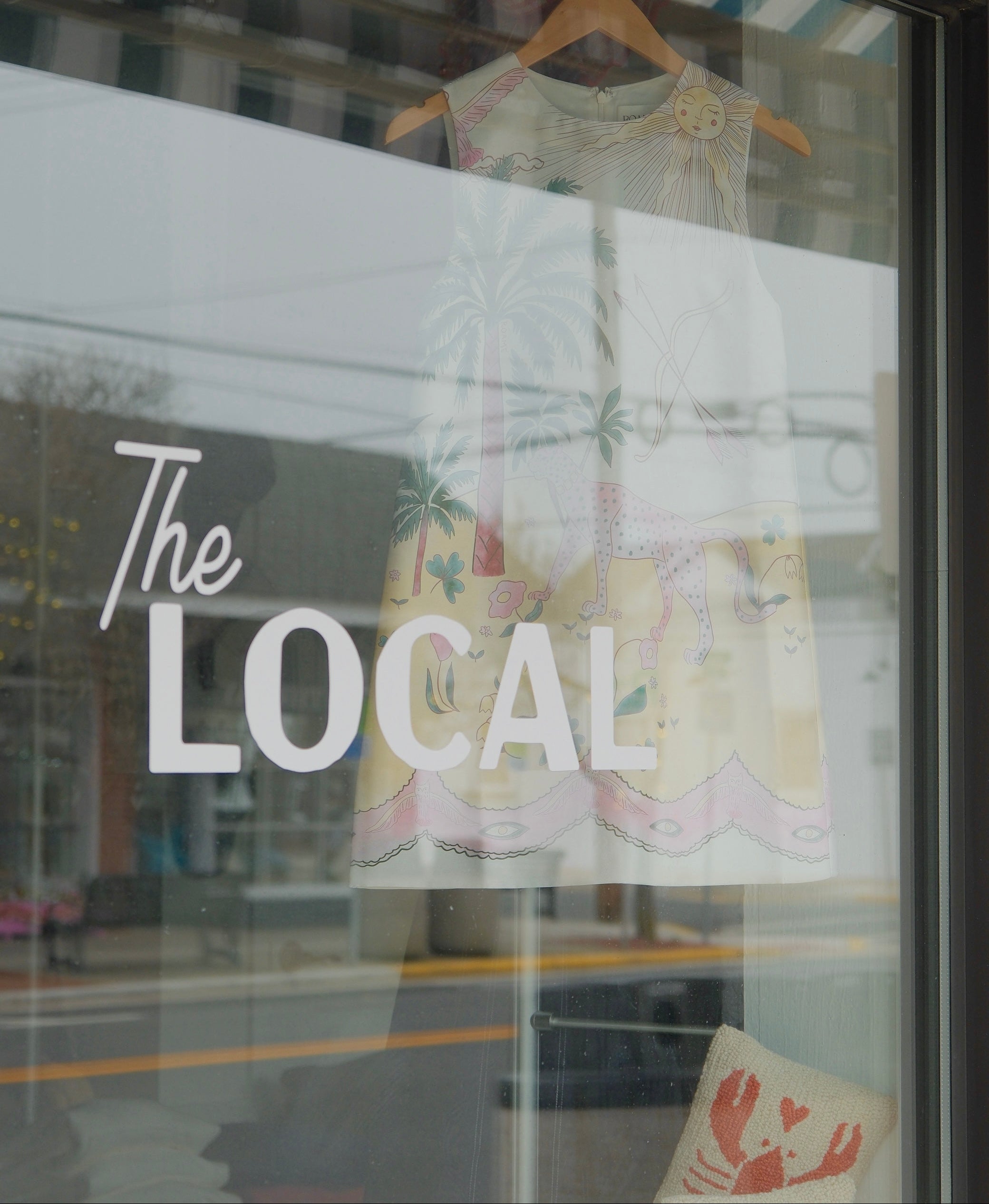 Storefront window with 'The Local' sign and a dress on a hanger
