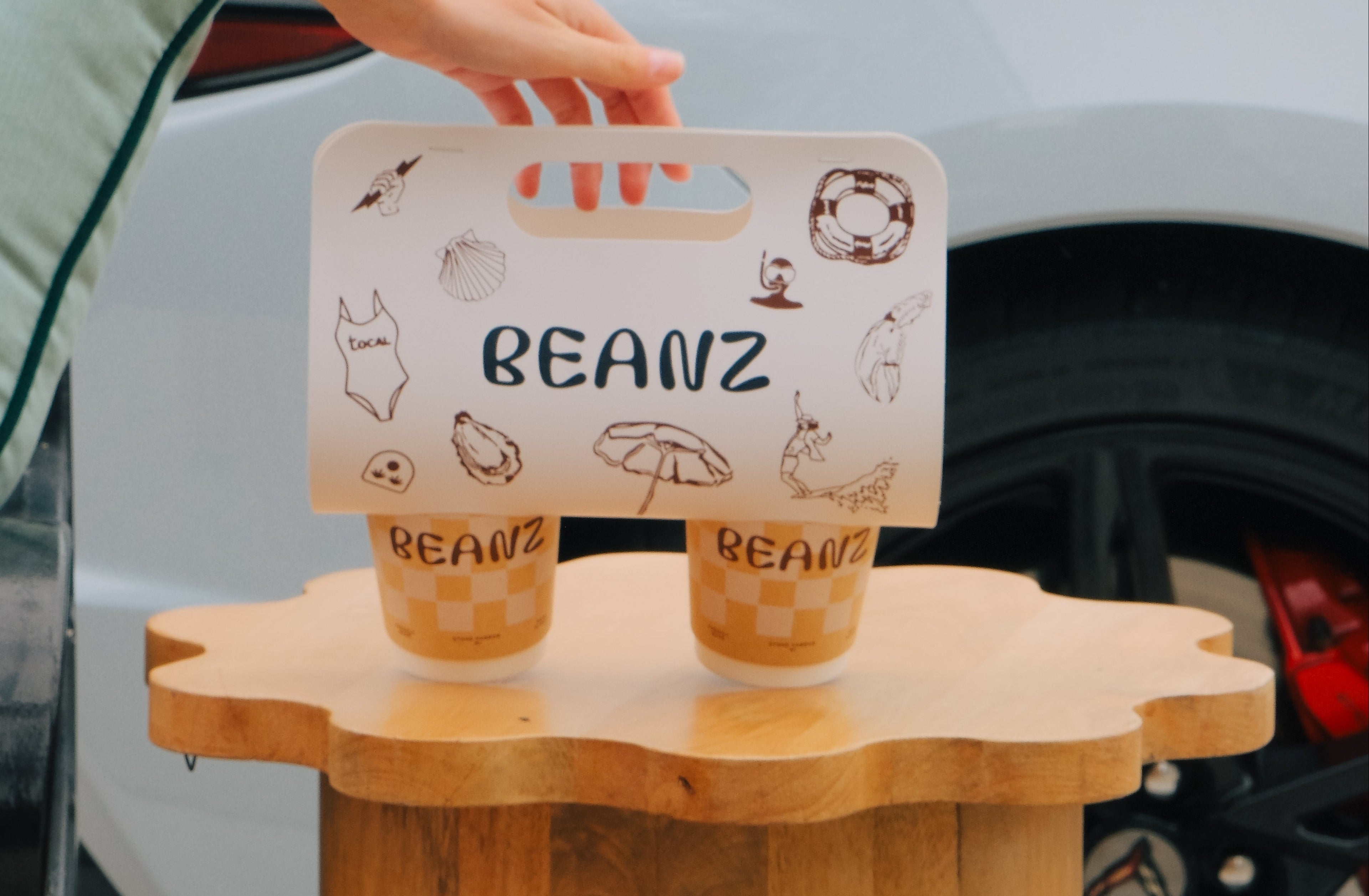 Person holding a 'BEANZ' product on a wooden stand with a car in the background